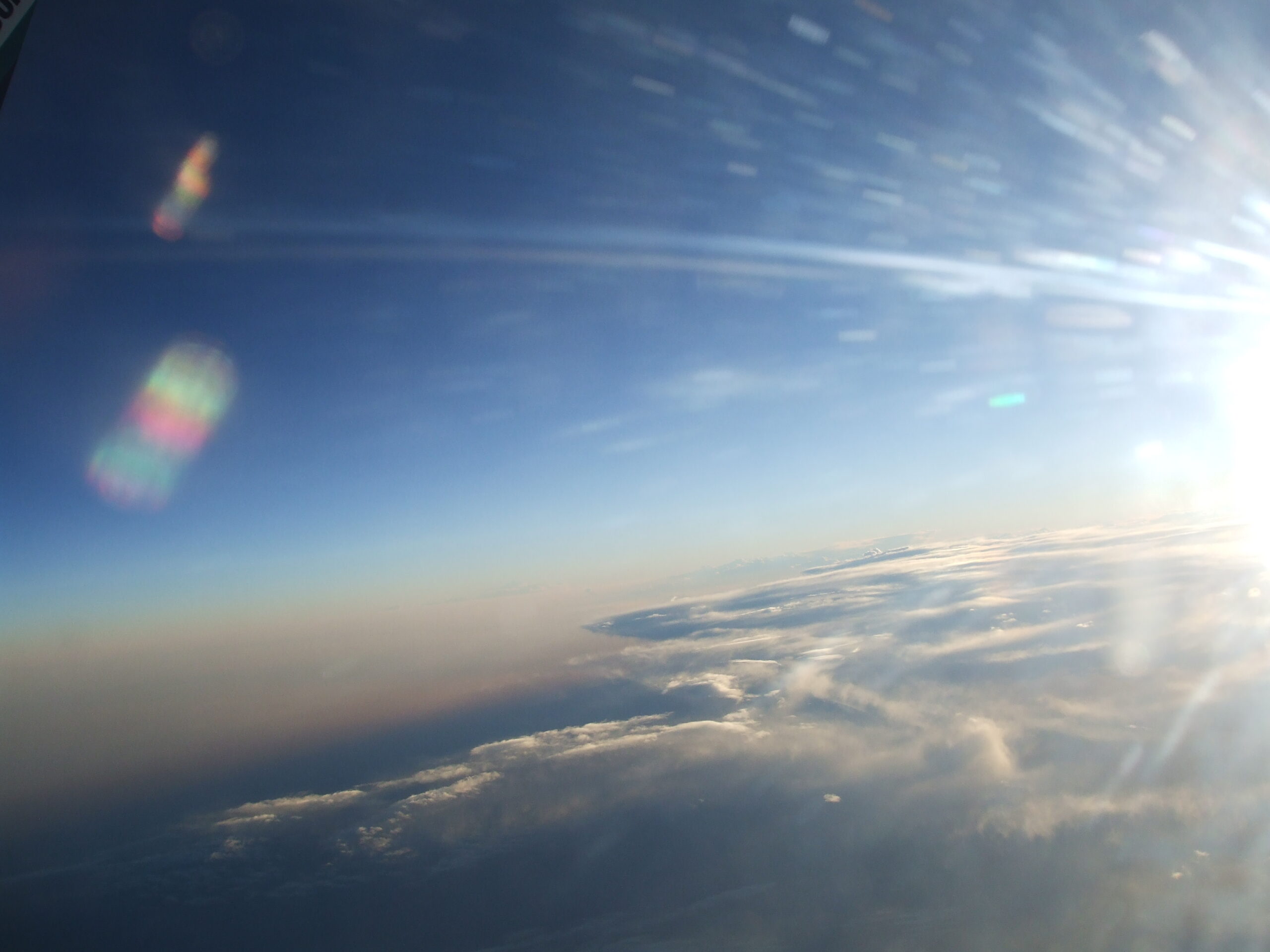 Aerial photo of frost on an airplane window. The sun to the right created 2 rainbow clusters to the left, over a beautiful landscape of rivers and land.